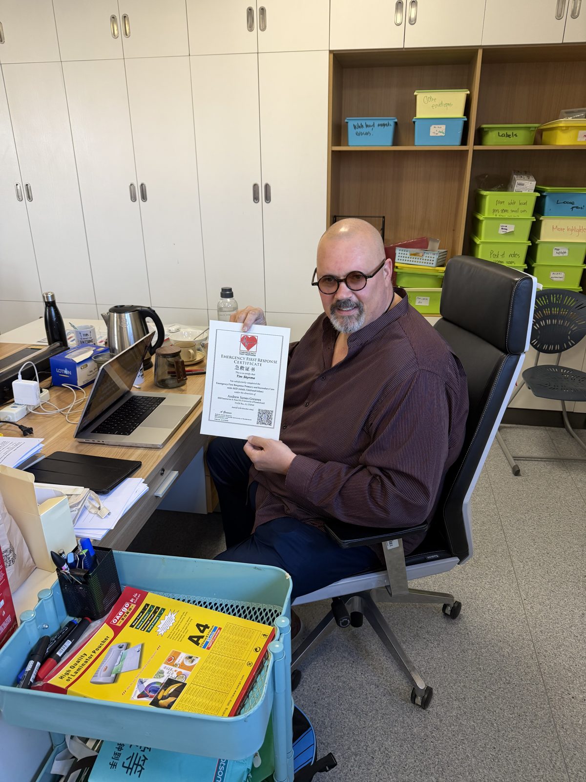 Newly qualified teacher at desk holding a UK Qualified Teacher Status certificate
